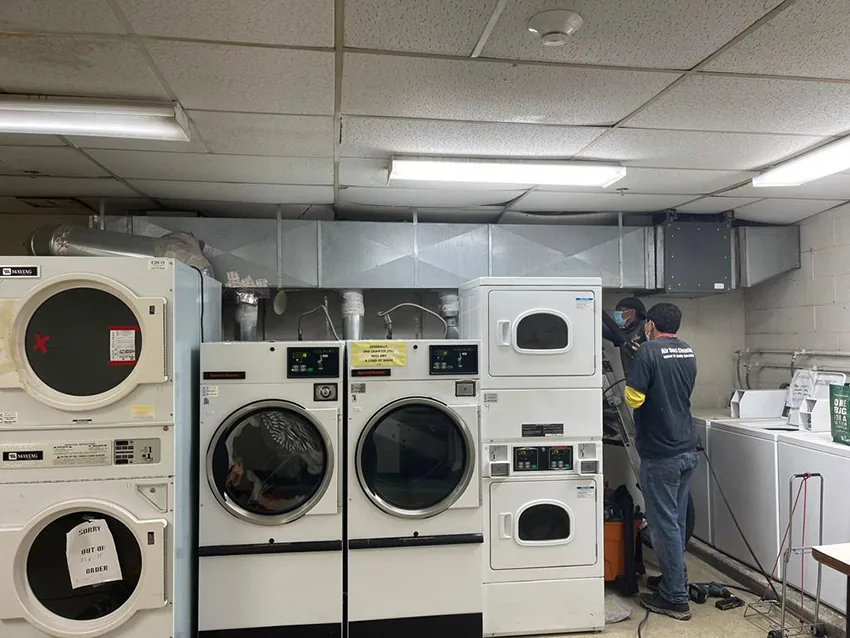 Technician cleaning commercial dryer vents in a laundromat
